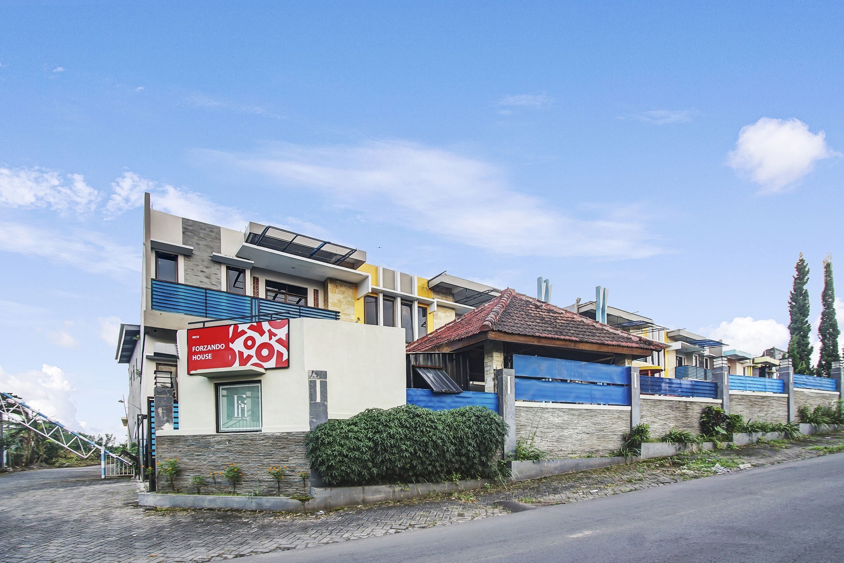A modern two-story house with a blue garage door, a solar panel on the roof, and a sign advertising a house for sale.