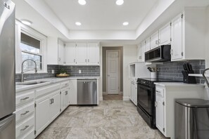 A modern kitchen with white cabinets, stainless steel appliances, and a tiled backsplash.