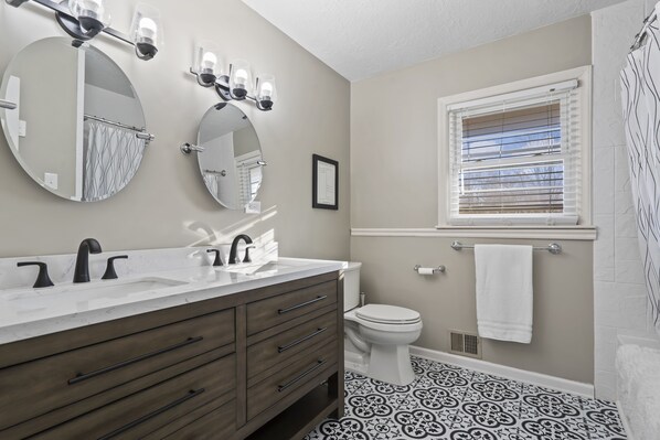 A bathroom with a double sink vanity, a toilet, and a shower area. - House in Lee's Summit (Lee's Summit)