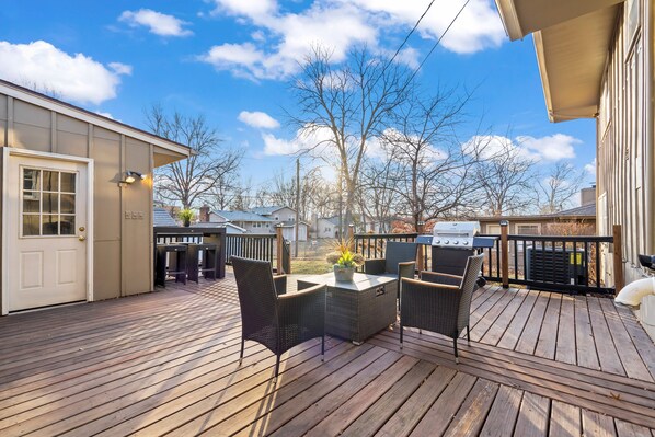 A wooden deck with outdoor furniture, a grill, and a view of neighboring houses.