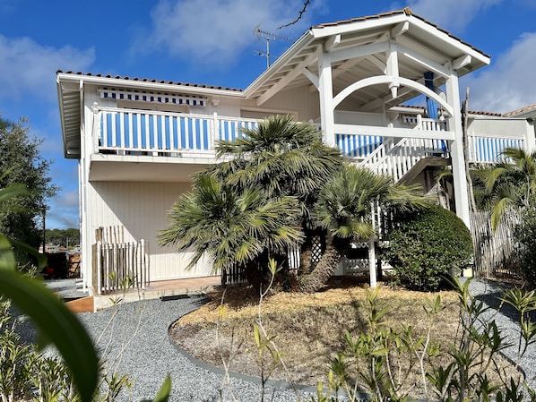 A two-story building with a white exterior and blue accents, featuring a covered porch and a staircase leading to the upper level. - A coastal vacation at Villa La Conche – with a view of the "Magical Basin" 🌟 (Lège-Cap-Ferret)
