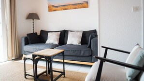 Een woonkamer met een grijze bank, een klein houten tafeltje en een lamp.