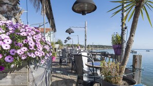 Een terras met tafels en stoelen, een hangende bloemdecoratie en uitzicht op het water.
