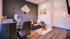 A modern living room with a grey sofa, a coffee table, and a dining area with chairs and a glass table. - 1 Bedroom apartment with an open plan kitchen, diner, and lounge. (York)