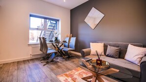 A modern living room with a grey sofa, a glass coffee table, and a dining area with a glass table and chairs. - 1 Bedroom apartment with an open plan kitchen, diner, and lounge. (York)