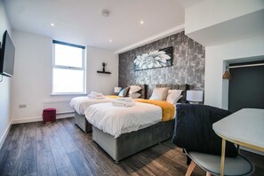 A modern bedroom with two beds, a large window, and a grey accent wall with a floral painting.