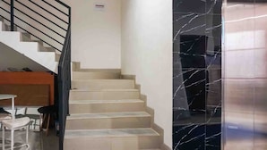 A staircase with beige steps leading to a landing, a black marble wall, and a metallic elevator door. - Collection O 91226 M'kostel Syariah (Sindangheula)