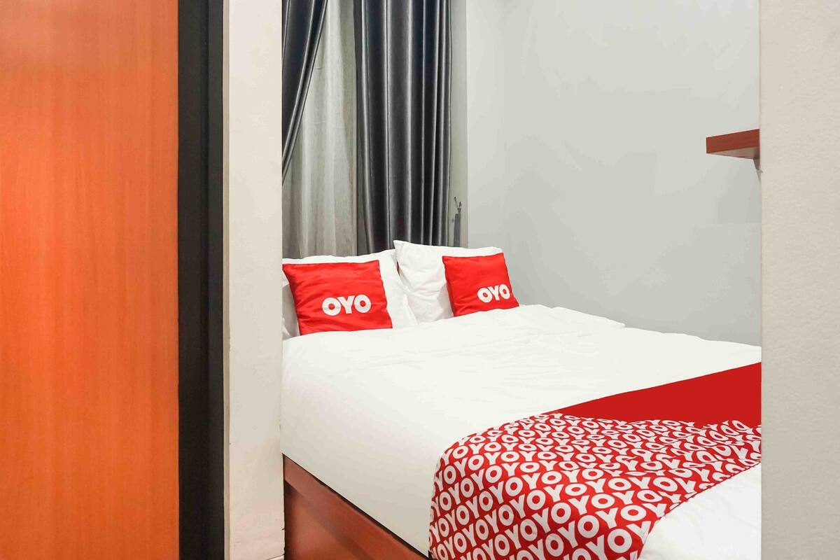 Une chambre d’hôtel avec un lit, une literie rouge et blanche, et une couverture à motifs rouges et blancs.