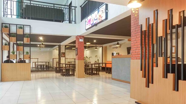 A spacious indoor area with a high ceiling, multiple seating arrangements, and a visible staircase leading to an upper level. - Collection O 91226 M'kostel Syariah (Sindangheula)
