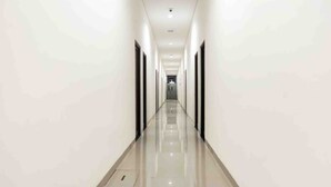 A long, narrow hallway with a shiny floor and white walls, leading to a door at the end. - Collection O 91226 M'kostel Syariah (Sindangheula)
