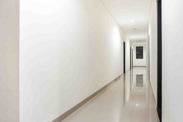 A long, narrow hallway with white walls and a shiny floor, leading to a door at the end. - Collection O 91226 M'kostel Syariah (Sindangheula)