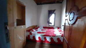 Una habitación con una cama, un armario de madera, un ventanal con cortinas y una puerta con pomo redondo.