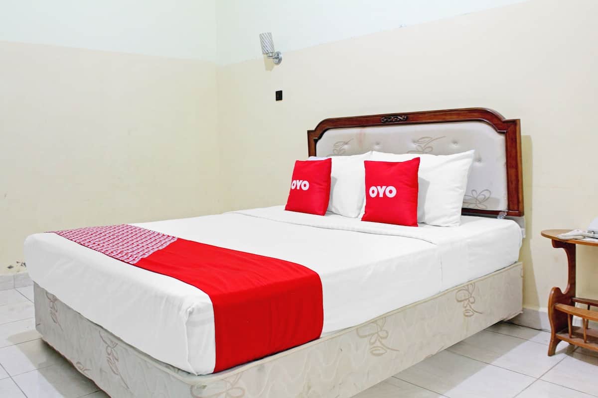 Ein ordentlich bezogenes Bett mit einer weiß-roten Tagesdecke, zwei rote Kissen mit dem Schriftzug "OYO" und ein Holz-Kopfstück.