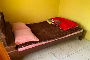 Una cama individual con un colchón marrón, almohadas estampadas en rosa y blanco, y una manta roja.