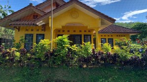Un bâtiment jaune, surmonté d’un toit en tuiles, entouré d’une végétation luxuriante.