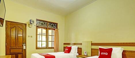 A hotel room with two beds, a wooden door, a window with curtains, and a bedside table.