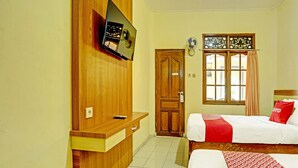 Habitación de hotel con un escritorio de madera, un televisor montado en la pared, una cama con ropa de cama roja y blanca y una ventana con cortinas.