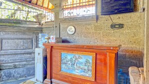 Un área de recepción con un escritorio de madera, un cuadro enmarcado, un dispensador de agua y una pared de piedra.