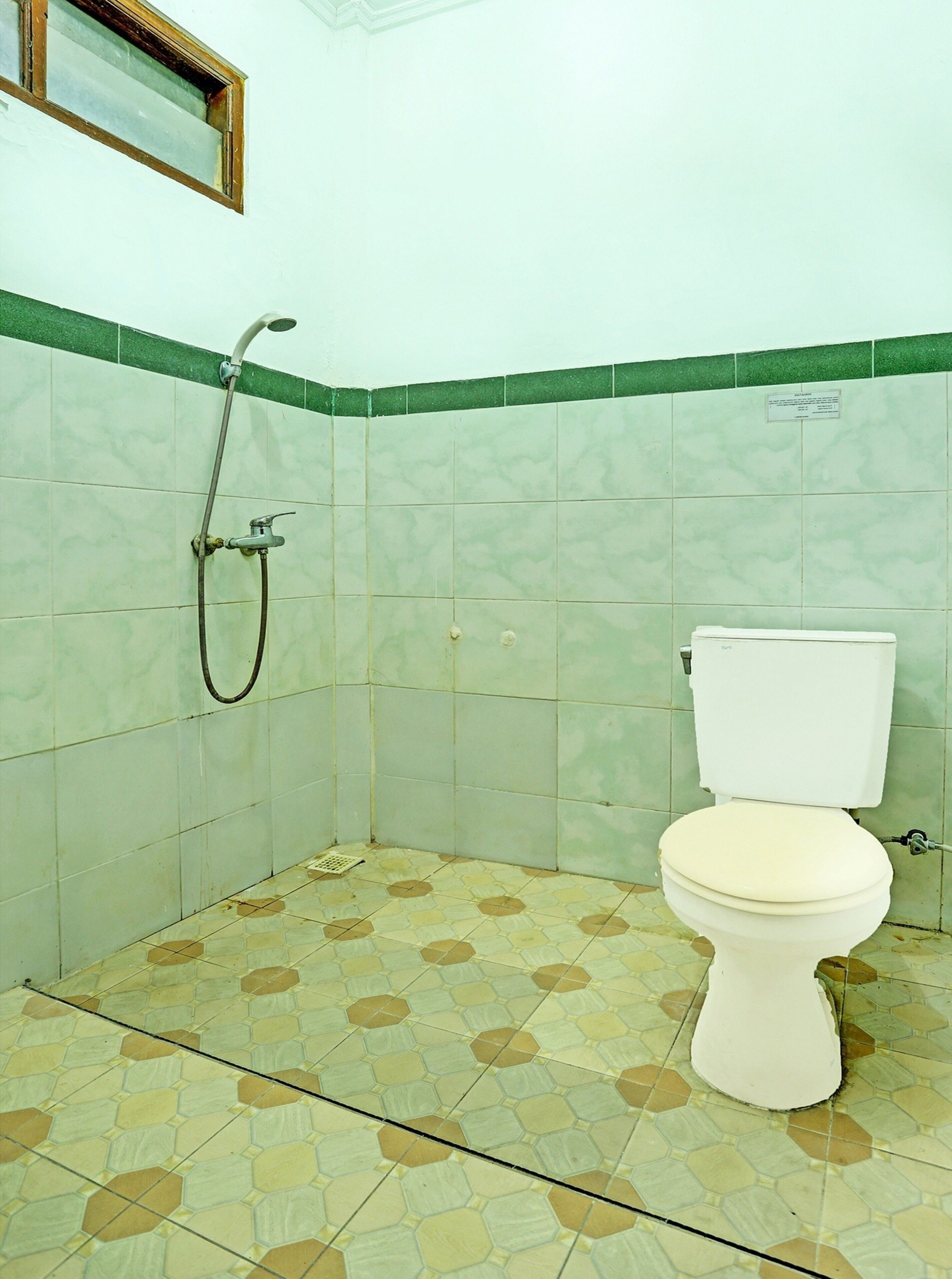 A bathroom with a toilet, shower, and green-tiled walls.