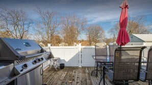 An outdoor deck with a barbecue grill, a table with chairs, and a covered umbrella. - Unique spacious upper Condo Suite. Steps from waterfront  (Sarnia)