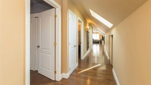A long, narrow hallway with wooden flooring and white doors, leading to a room with a large window. - Unique spacious upper Condo Suite. Steps from waterfront  (Sarnia)