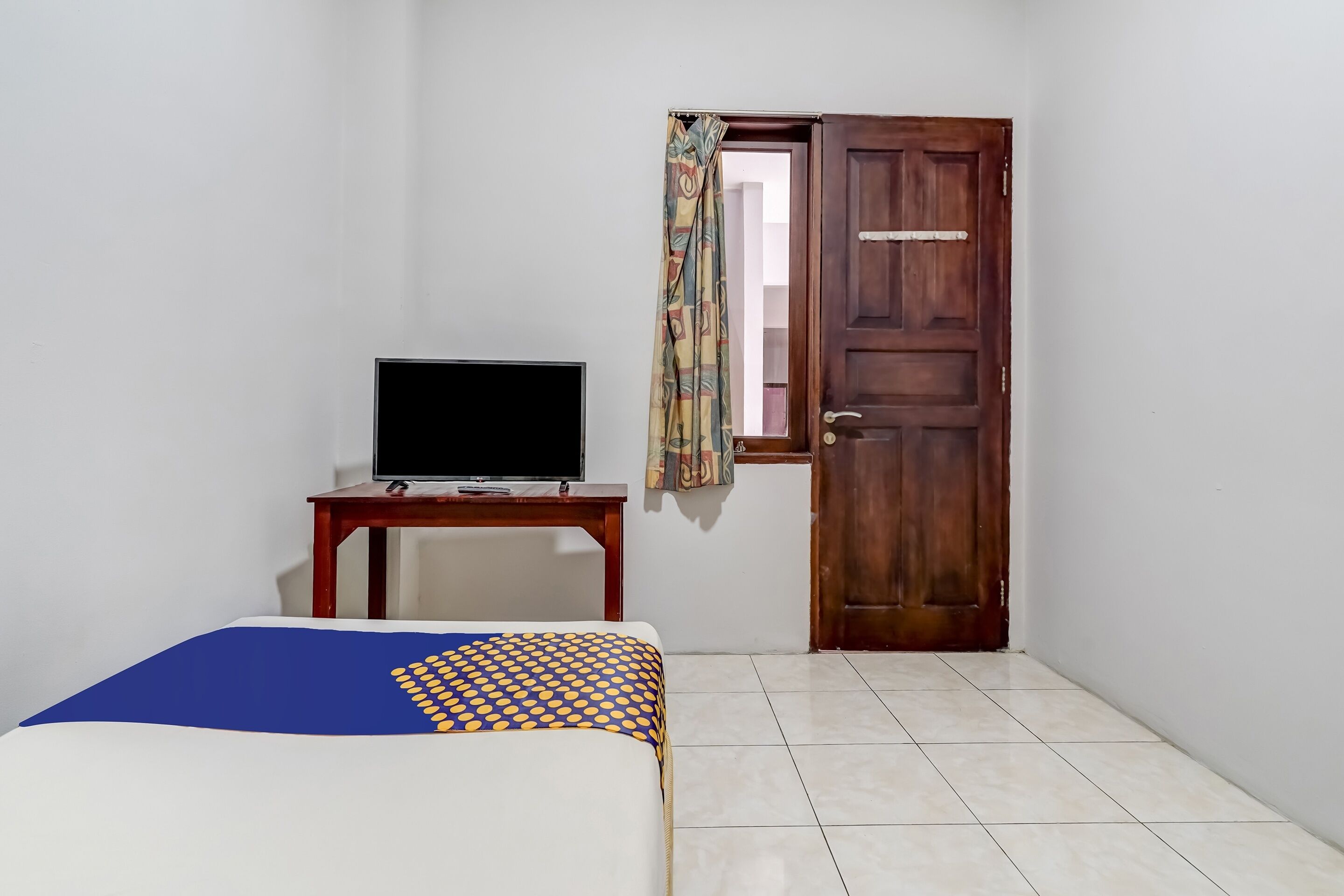 A room with a bed, a television on a small table, and a wooden door.
