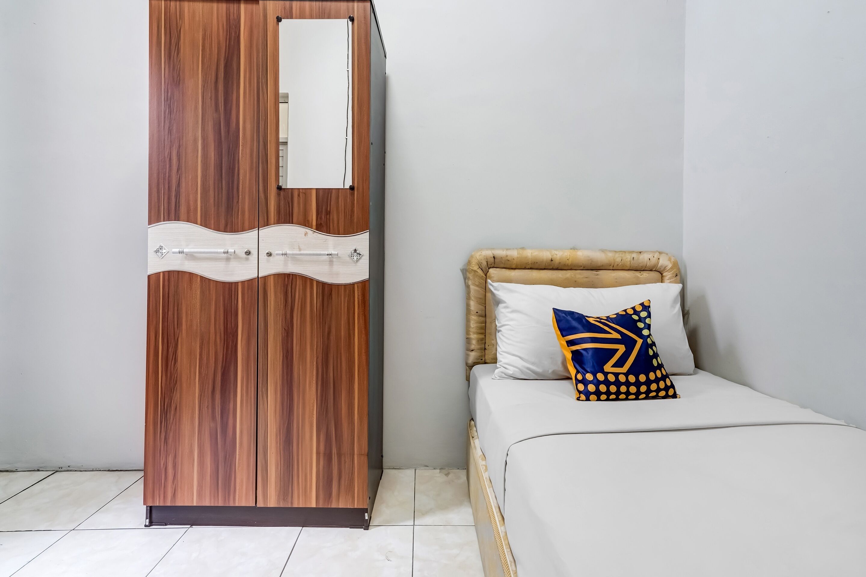 Une chambre avec une armoire en bois, un lit avec une literie blanche et un seul coussin décoratif.