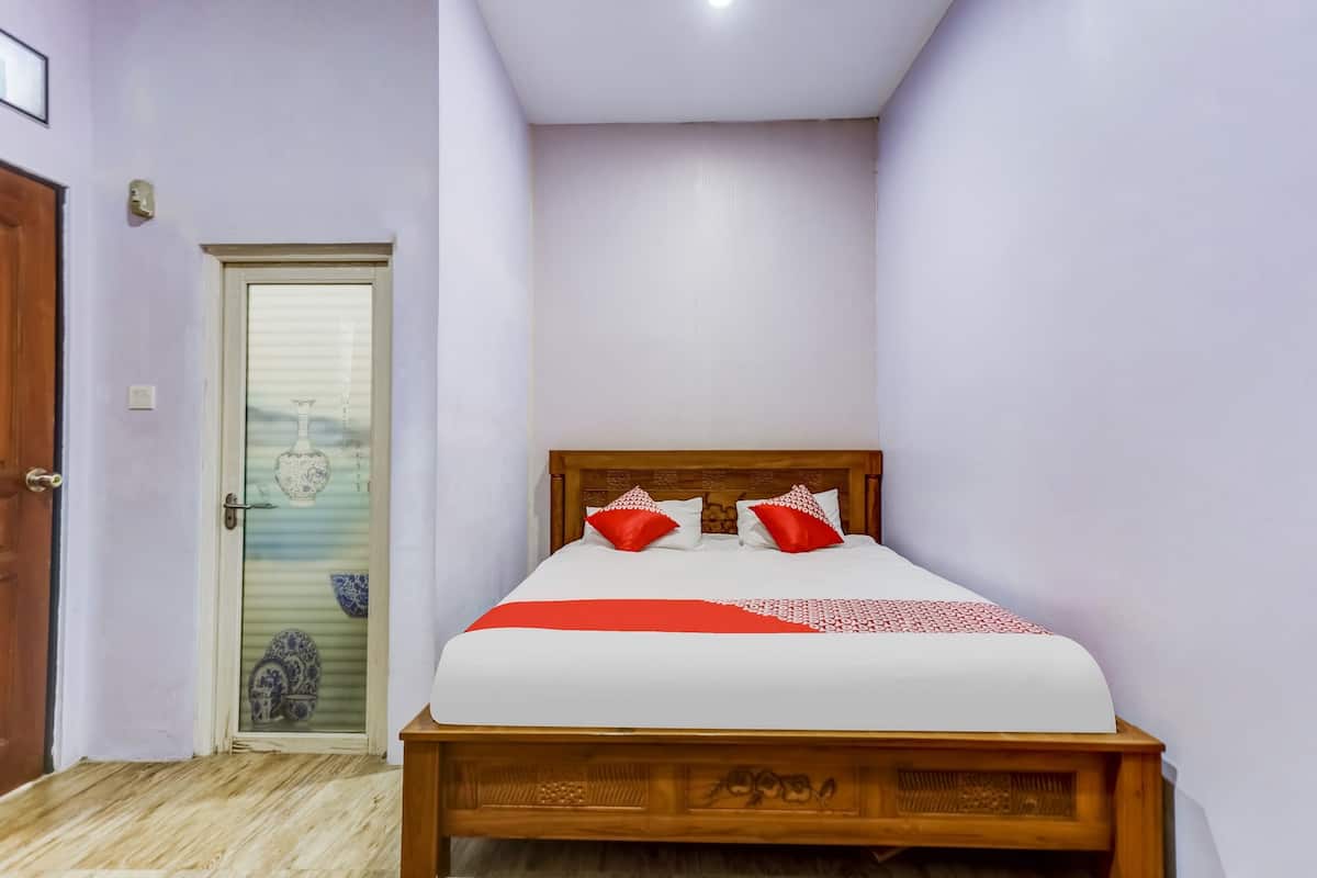 Un dormitorio con una cama de madera, una puerta con panel de vidrio y un pequeño objeto decorativo en el suelo.