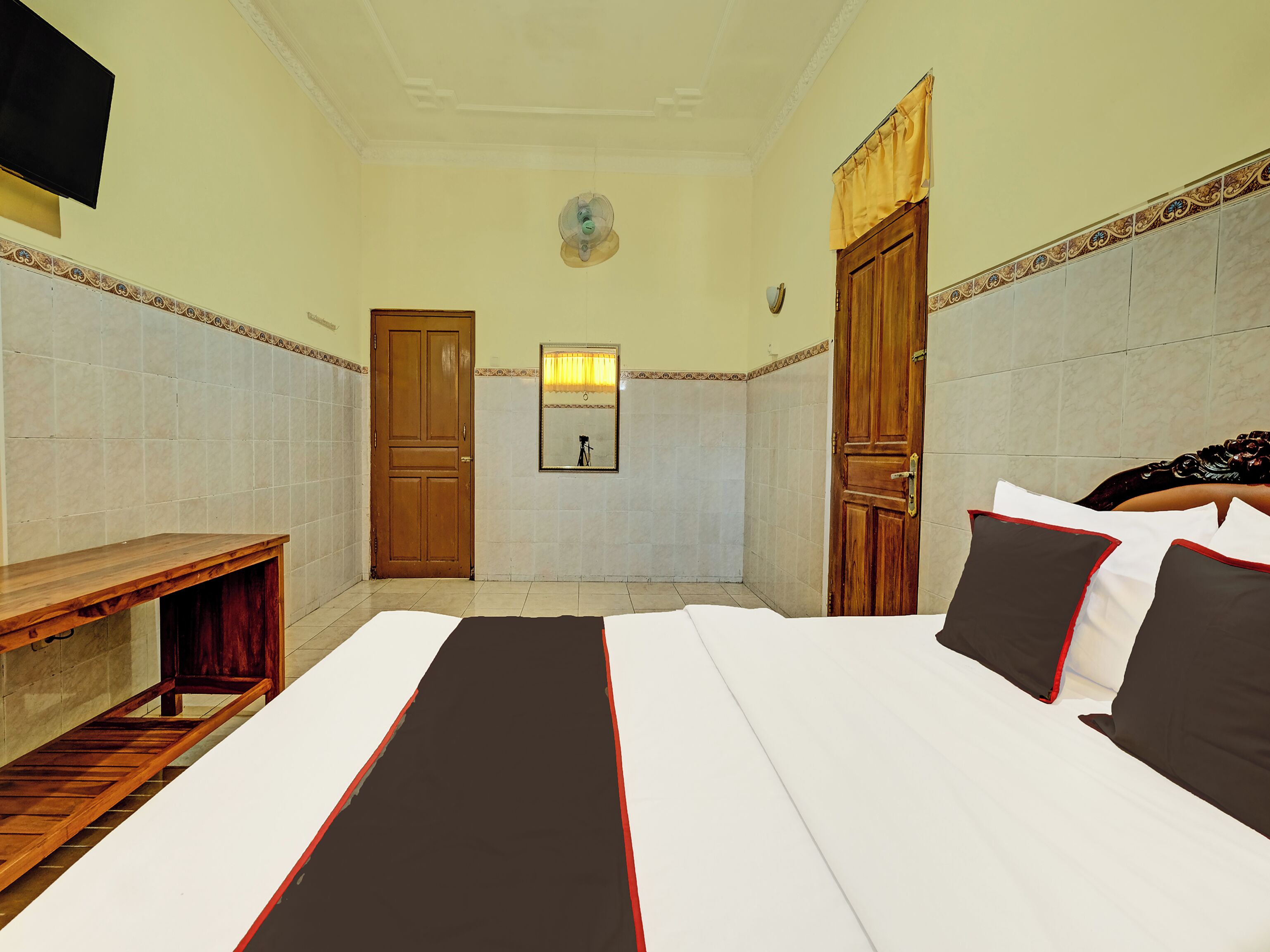 A hotel room with a bed, a wooden bench, a mirror, and two doors.