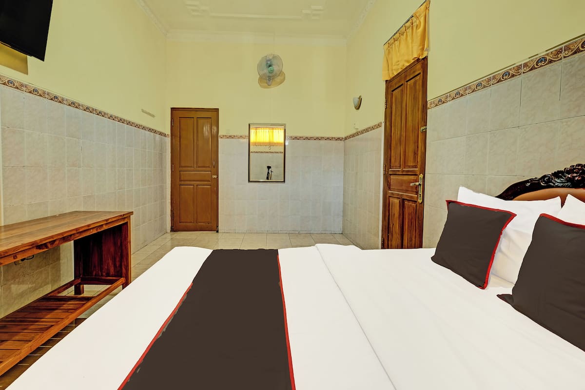 A hotel room with a bed, a wooden bench, a mirror, and two doors.