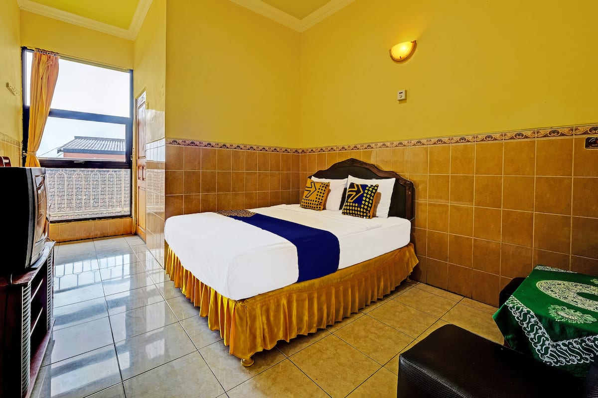 A hotel room with a bed, a television, a window with curtains, and a view of buildings outside.