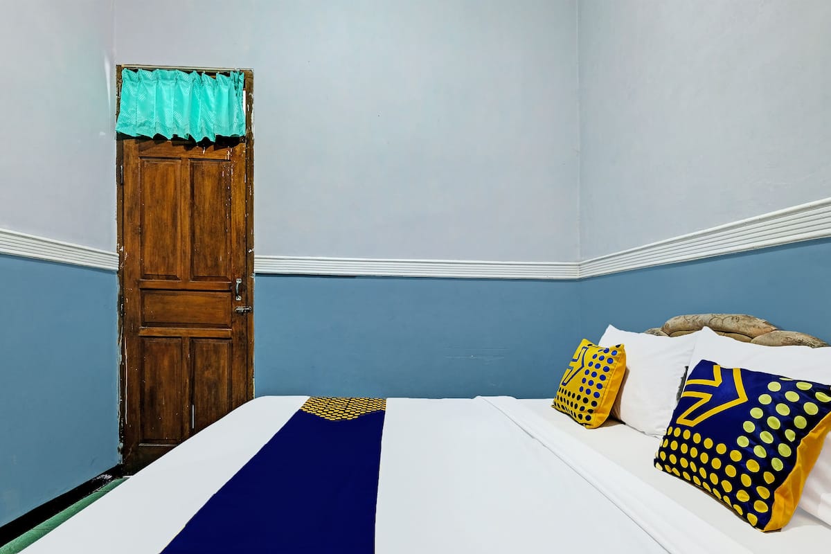 A bedroom with a wooden door, a blue wall, and a bed with white bedding and decorative pillows.