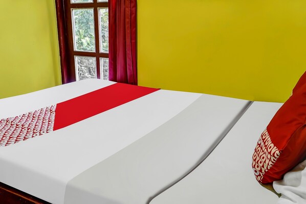 Una cama con una colcha blanca y roja, un almohárraga roja y una ventana con cortinas rojas.