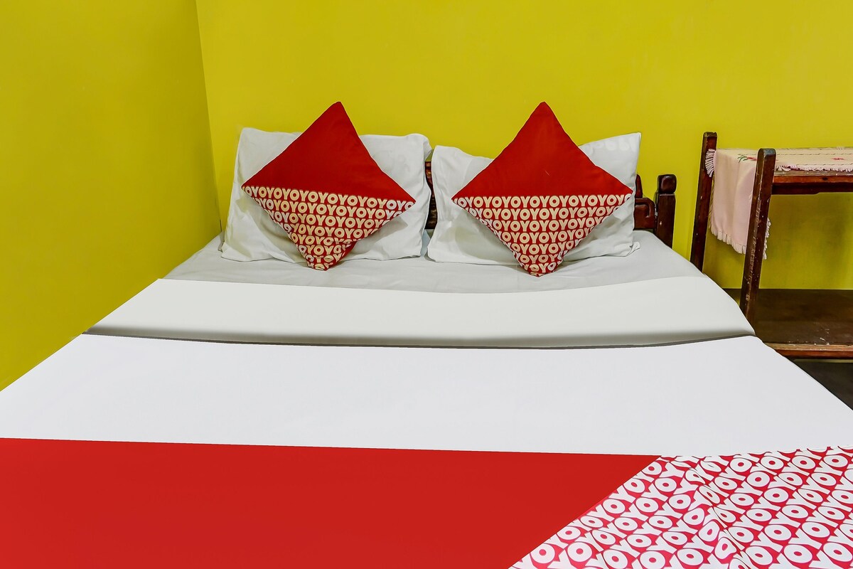 Un lit avec une literie blanche et deux oreillers rouges ornés d’un motif répété.