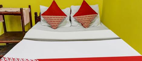 A bed with two pillows, a wooden chair, and a table against a yellow wall.