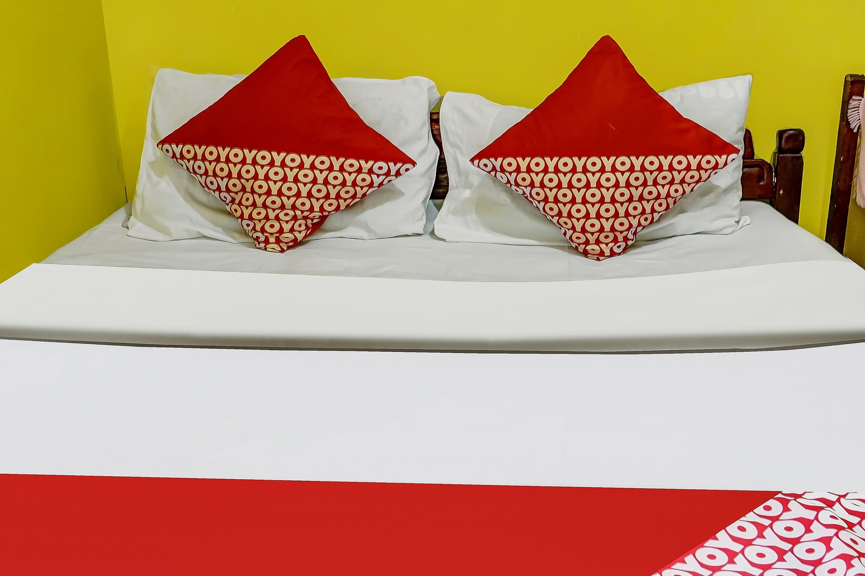 A bed with white bedding and two red pillows with a repeated pattern.