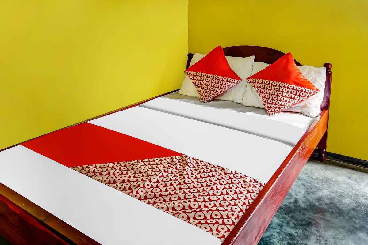 Ein Bett mit einer weiß-rot gemusterten Tagesdecke, zwei roten Kissen und einem Holzkopfende.
