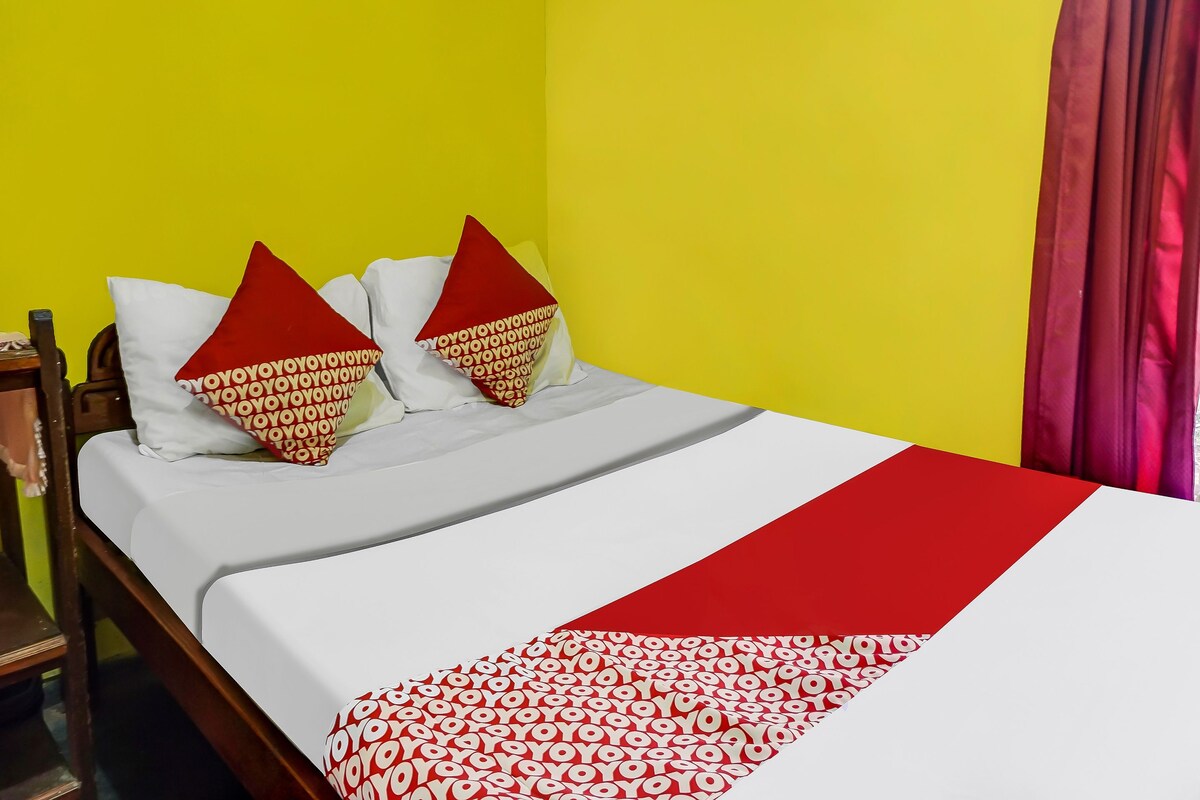 Ein Bett mit einer weiß-rot gemusterten Tagesdecke, zwei Kissen mit einem roten und weißen Muster und eine gelbe Wand.