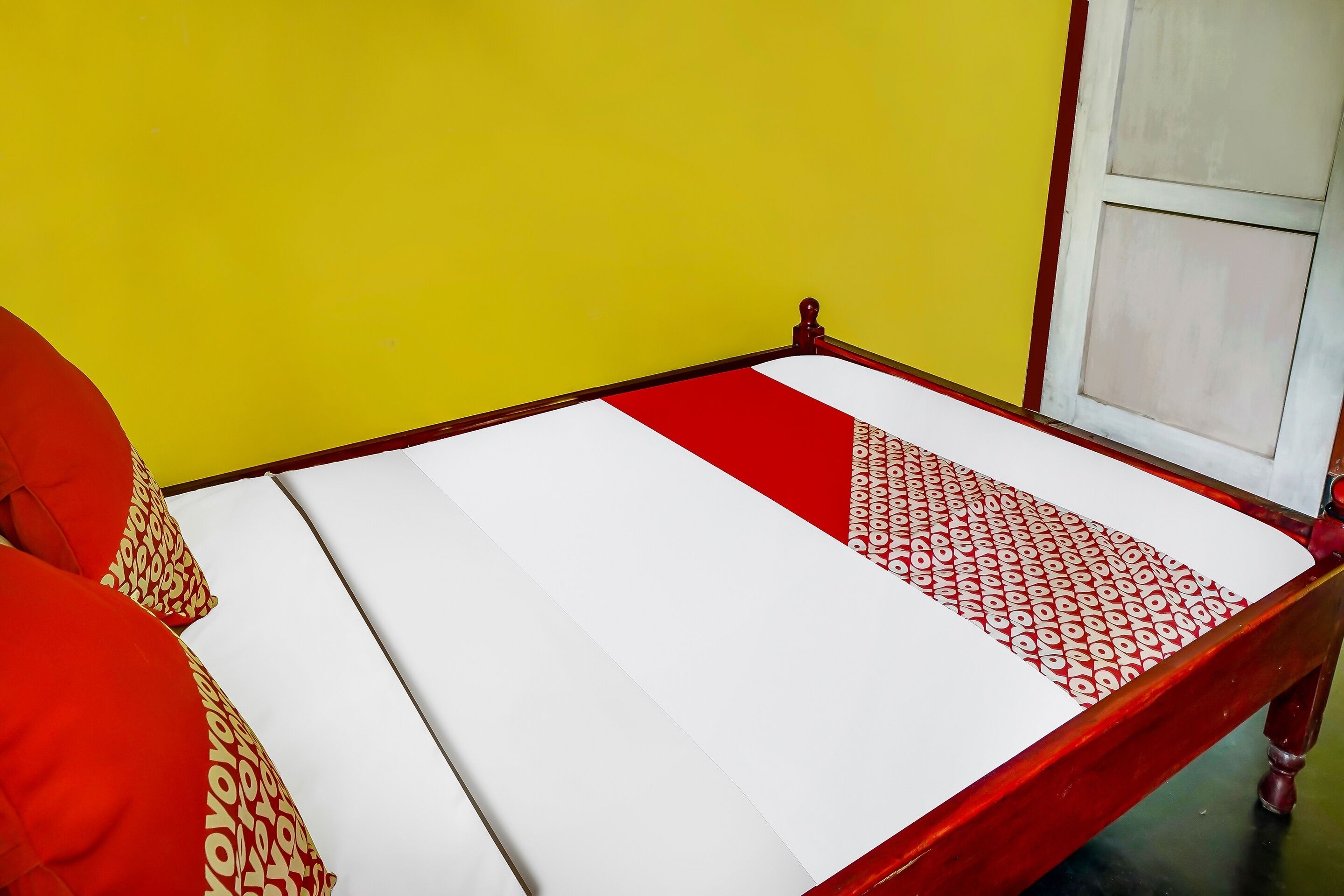 Una cama con colchón blanco y almohadas de estampado rojo y blanco, frente a una pared amarilla.