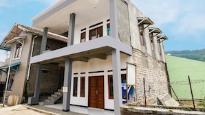 A two-story building with a balcony, a wooden door, and a staircase leading to the entrance. - OYO Homes 91008 Eco Tourism Desa Cibodas Babakan Gentong 1 Syariah (Lembang)