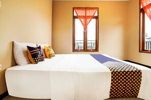 A neatly made bed with white and patterned bedding, a window with orange curtains, and a balcony view. - OYO Homes 91008 Eco Tourism Desa Cibodas Babakan Gentong 1 Syariah (Lembang)
