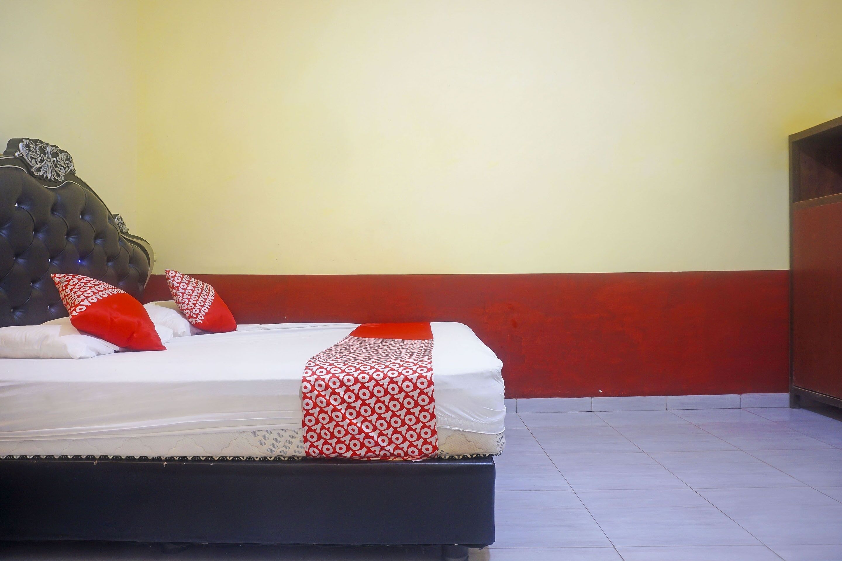 Una cama con colcha estampada, dos almohadas rojas y un cabecero acolchado.