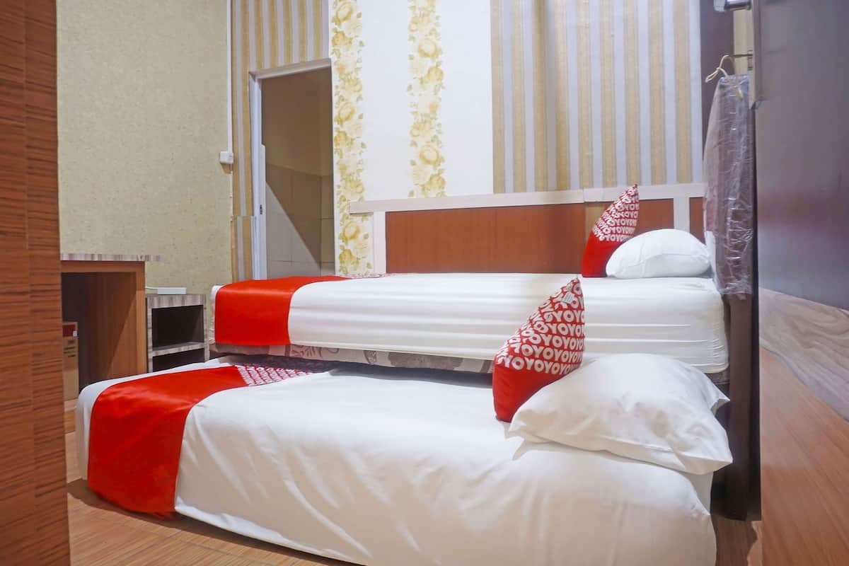 A hotel room with two beds, a wooden headboard, a small bench, and a mirror.