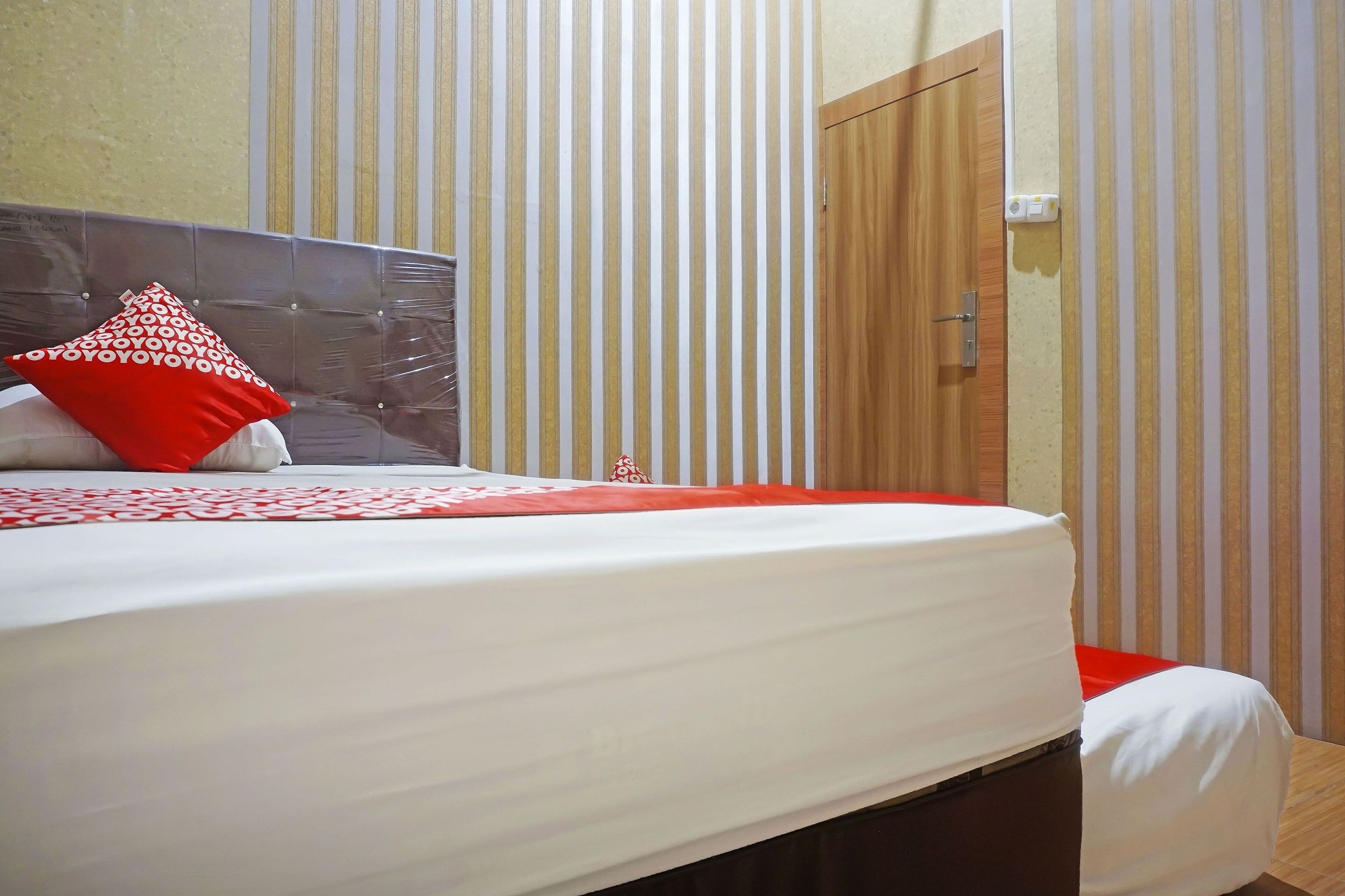 Een netjes opgemaakt bed met een wit-rode spreideken, een kussen met een rood-wit patroon, en een houten hoofdbord.