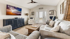Un salon comprenant un canapé, un fauteuil et une table basse. On y trouve également un ventilateur de plafond, un tableau accroché au mur et un meuble.