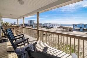 A wooden deck with chairs and a bench overlooking a beach with houses and a clear sky.