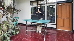 A person standing by a table with a laptop, a wooden door, and a window with curtains. - OYO Homes 91009 Eco Tourism Desa Cibodas Areng 4 Syariah (Lembang)