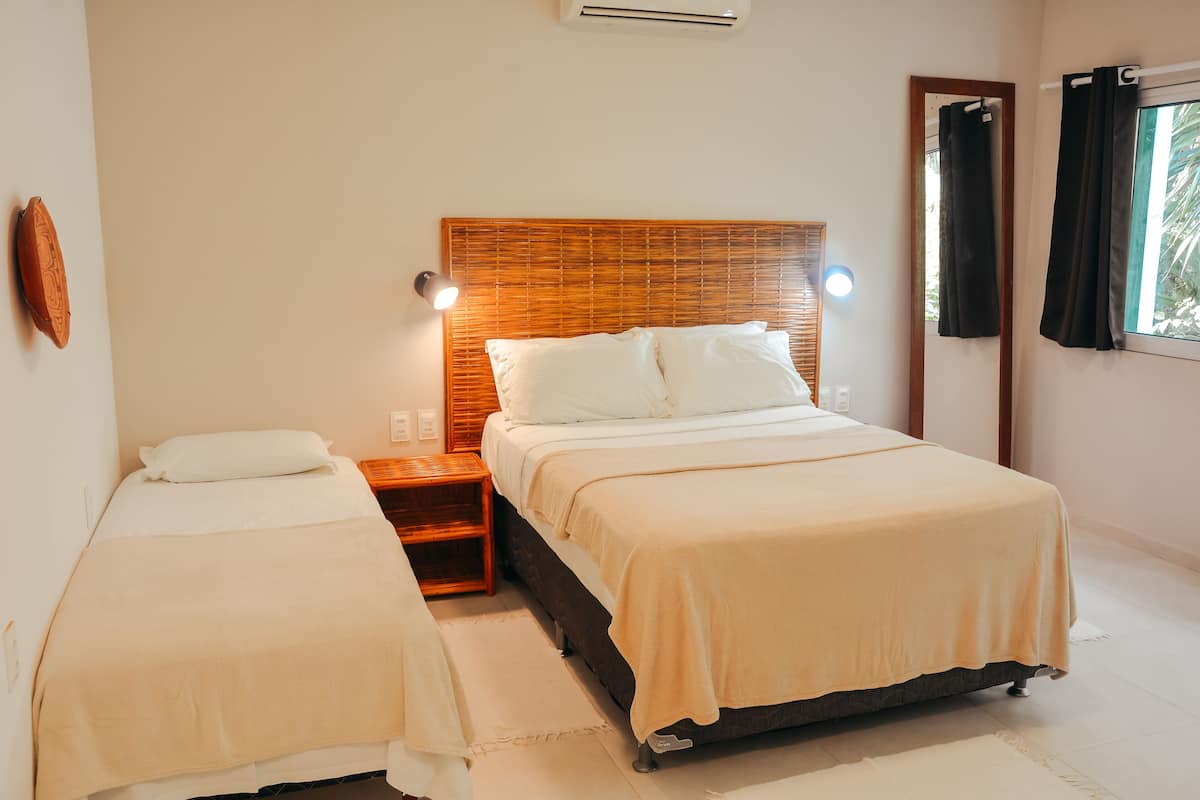 A hotel room with two single beds, a wooden headboard, bedside lamps, a nightstand, and a window with curtains.
