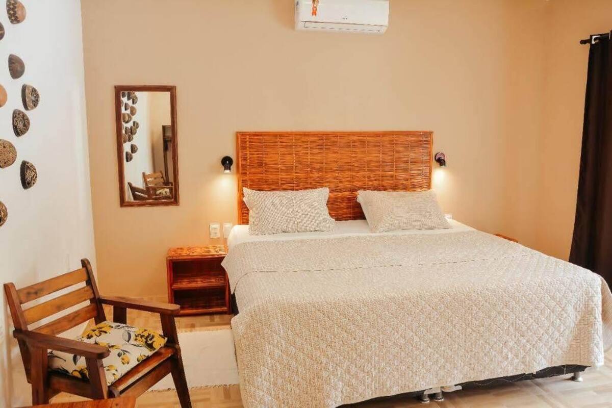 A neatly arranged bedroom with a large bed, a wooden nightstand, a chair, and a mirror on the wall.