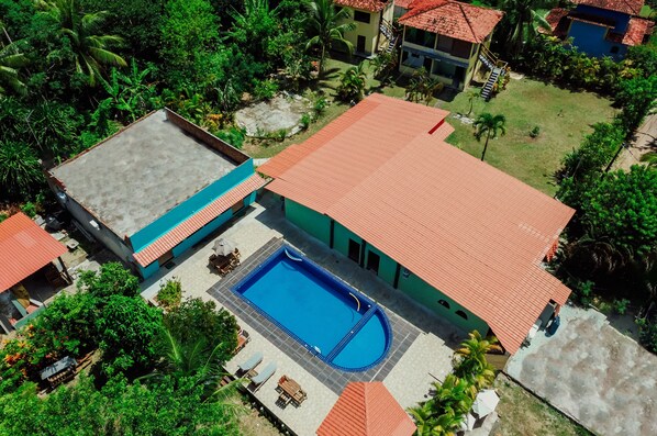 Vista aérea de una propiedad con piscina, un patio cubierto y follaje circundante.
